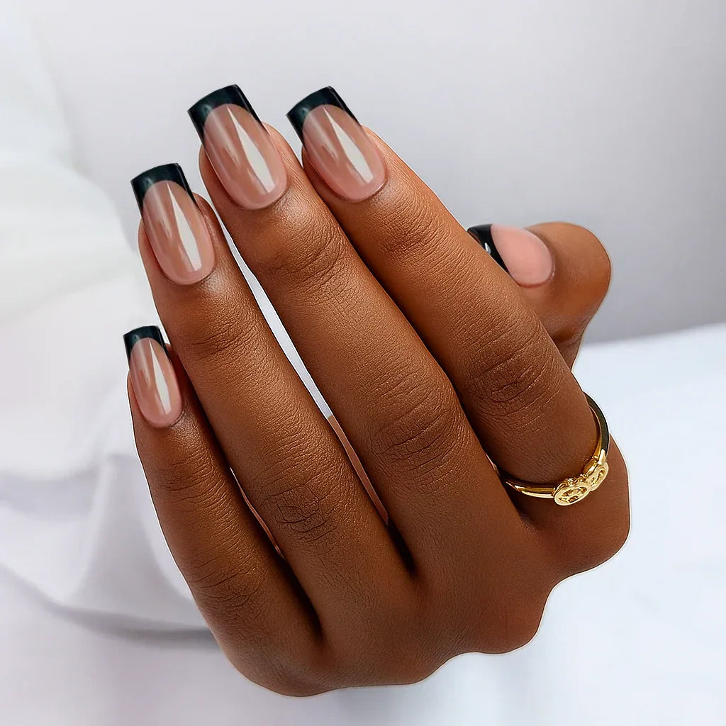 Elegant nude nails with black tips, showcasing a stylish manicure on a hand with a gold ring.