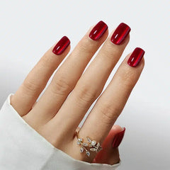 Elegant red nail polish on manicured nails, featuring a delicate gold ring with gem accents.