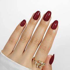 Close-up of manicured hands with glossy burgundy nail polish and a gold floral ring.