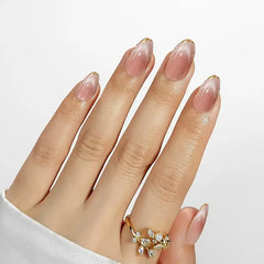 Elegant pink ombre stiletto nails with gold tips, showcasing a chic floral ring on a hand.