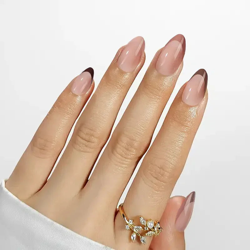 Elegant nude gradient stiletto nails with dark tips, showcasing a stylish gold ring with floral embellishments.