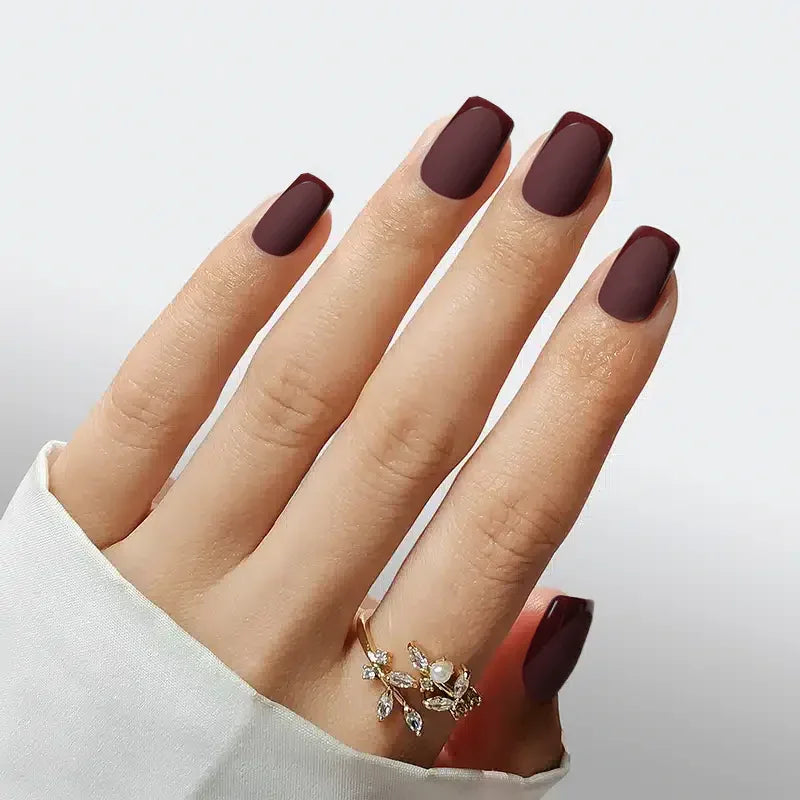 Matte burgundy acrylic nails adorned with a stylish gold ring, perfect for elegant looks.