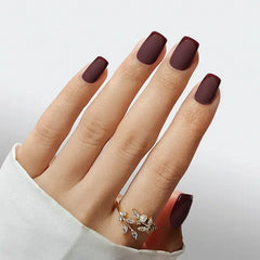Matte burgundy acrylic nails adorned with a stylish gold ring, perfect for elegant looks.
