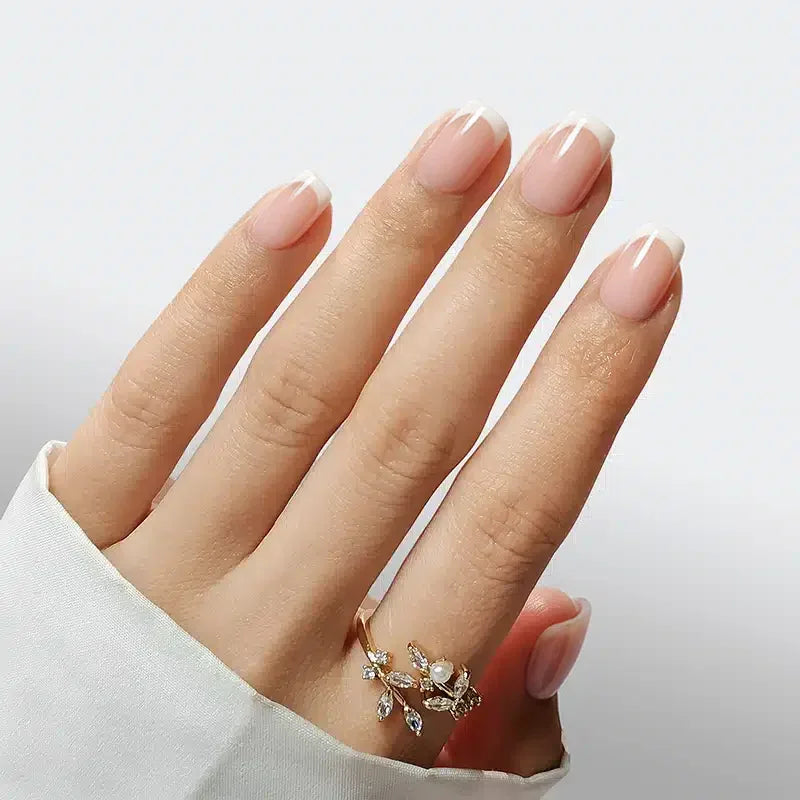 Elegant manicured nails in nude with white tips, showcasing a delicate gold floral ring.