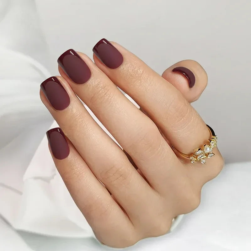 Chic matte burgundy nails with a gold flower ring, perfect for elegant occasions.