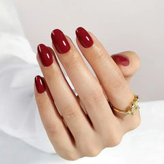 Elegant deep red nail polish on long almond-shaped nails, highlighting a gold ring with sparkling stones.