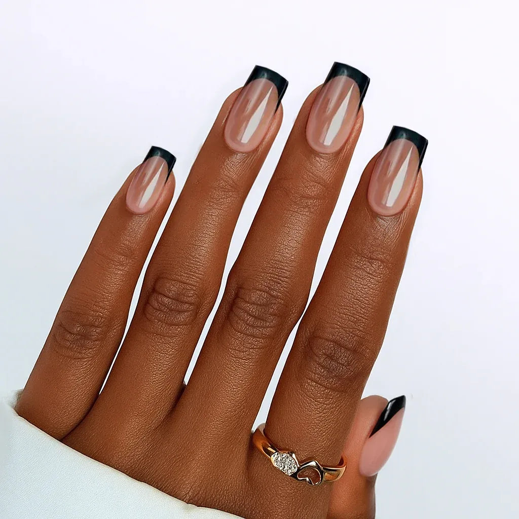 Elegant nude nails with black tips, showcasing a stylish manicure on a hand with a gold heart ring.