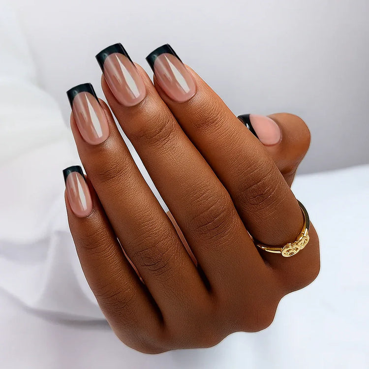 Elegant nude nails with black tips, showcasing a stylish manicure on a hand with a gold ring.
