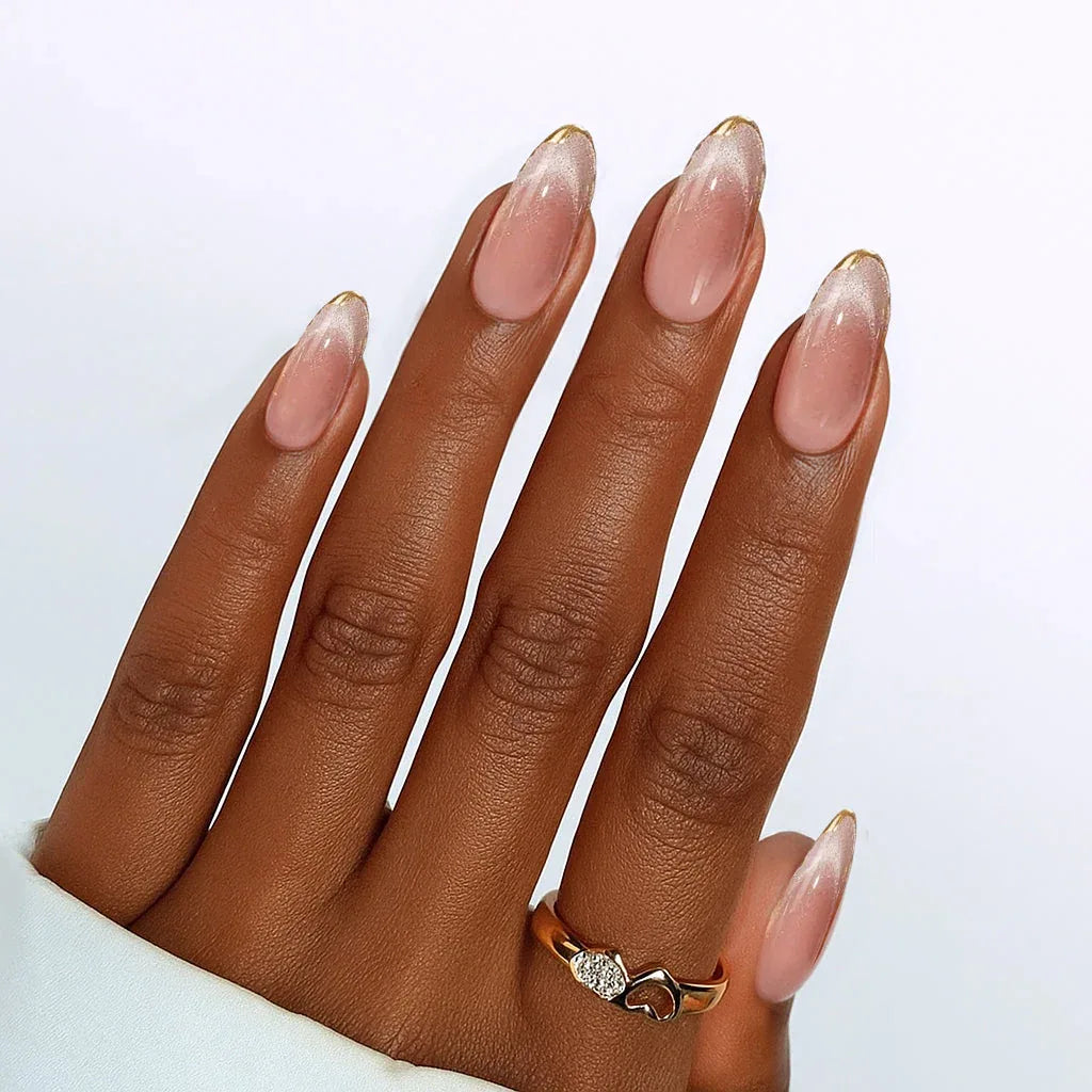 Elegant pink ombre acrylic nails with gold tips and a stylish gold heart ring.
