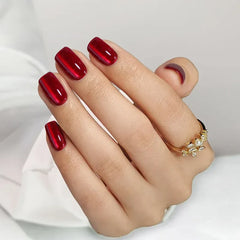 Glossy red nail polish on manicured nails, featuring a modern oval shape, complemented by a gold ring.