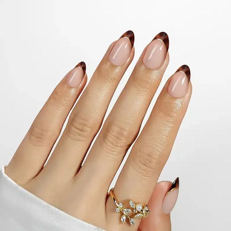 Nude French tip nails with brown tips, showcasing elegant hand wearing a gold floral ring.