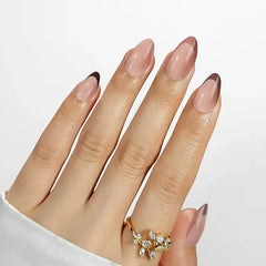 Elegant nude gradient stiletto nails with dark tips, showcasing a stylish gold ring with floral embellishments.