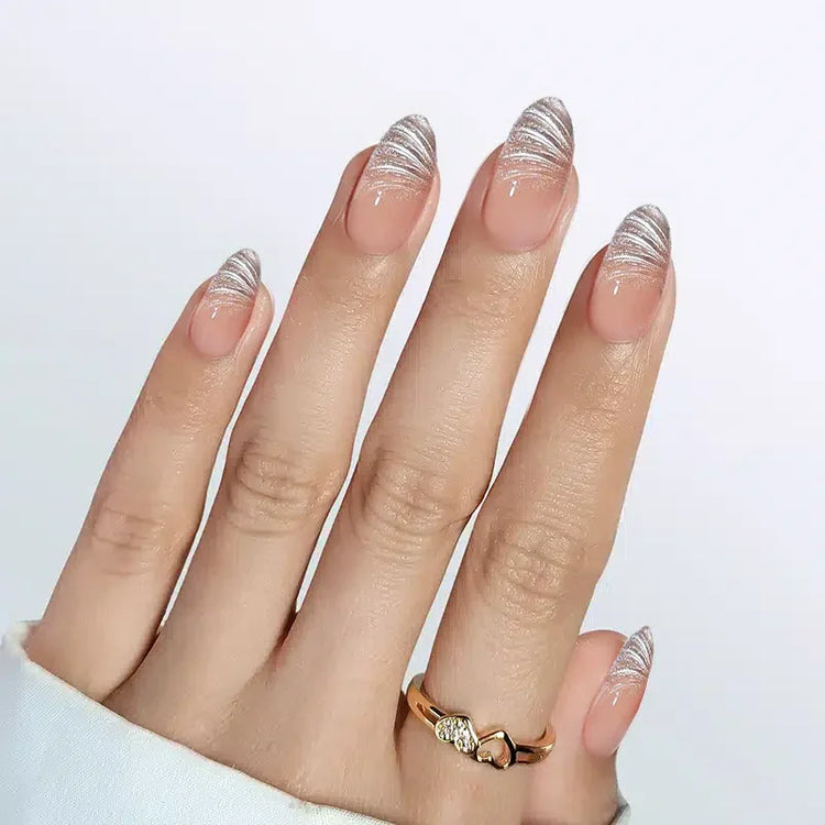 Elegant nude nails with silver abstract tips, showcasing stylish nail art and a gold ring accent.
