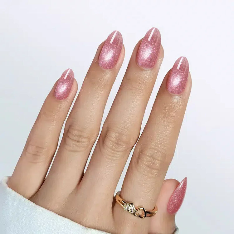 Sparkly pink almond-shaped nails with white stripes, showcasing a stylish gold ring on the hand.