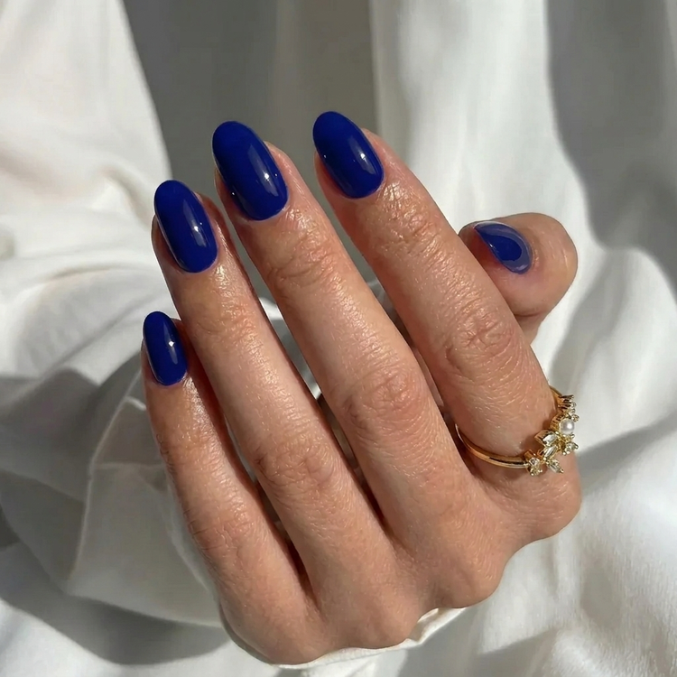 Navy blue oval press-on nails in a glossy finish, shown in a complete manicure set of various sizes