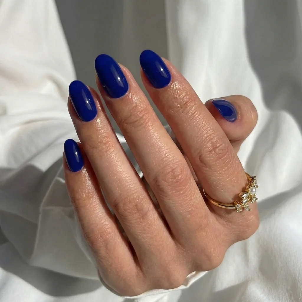 Navy blue oval press-on nails in a glossy finish, shown in a complete manicure set of various sizes