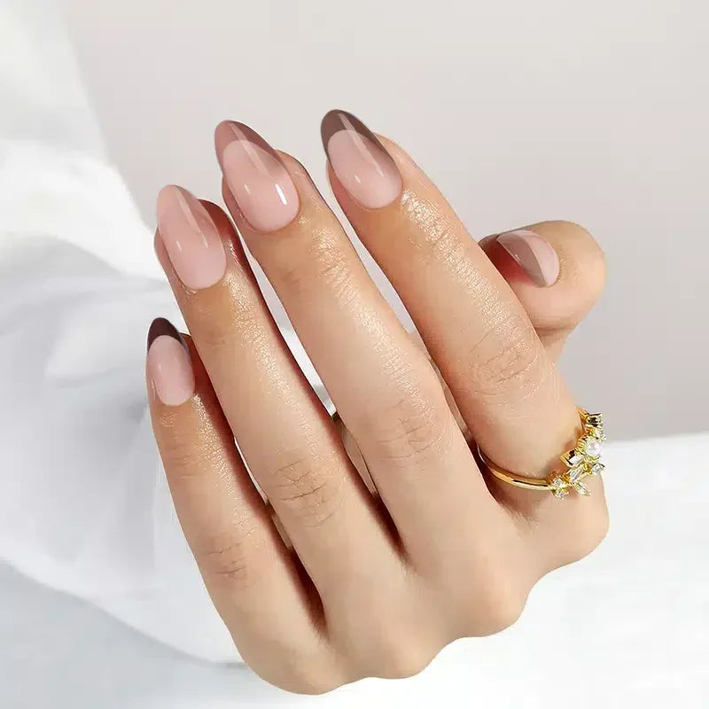 Elegant nude almond nails with brown tips, showcasing a chic manicure and gold ring accent.